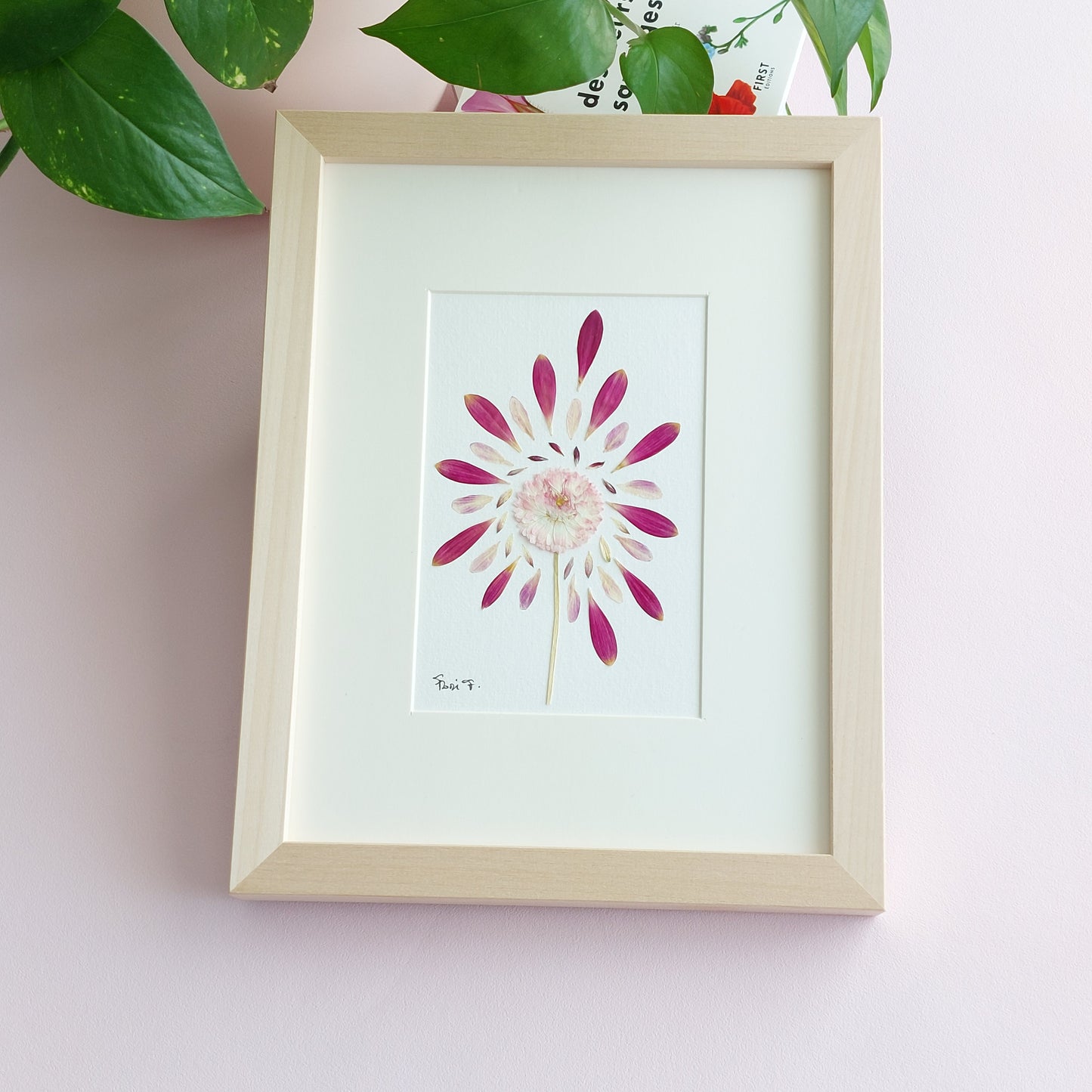 Partie de la collection Les Expressifs, cet herbier d'art encadré a été réalisé avec une marguerite anglaise à tige, sublimée par de magnifiques pétales de dahlia rose, de gerbera et d'Astrantia de provenance locale.