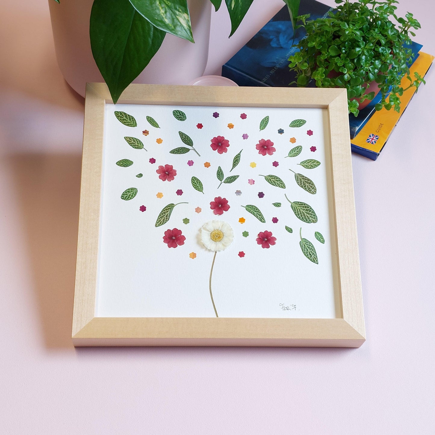 Herbier d'art au format 20/20 cm, composé d'une marguerite anglaise à tige, accompagnée d'une envolée de verveinerouges et des feuillesvertes. Cadre en bois de tilleul haut de gamme fabriqué en Italie.