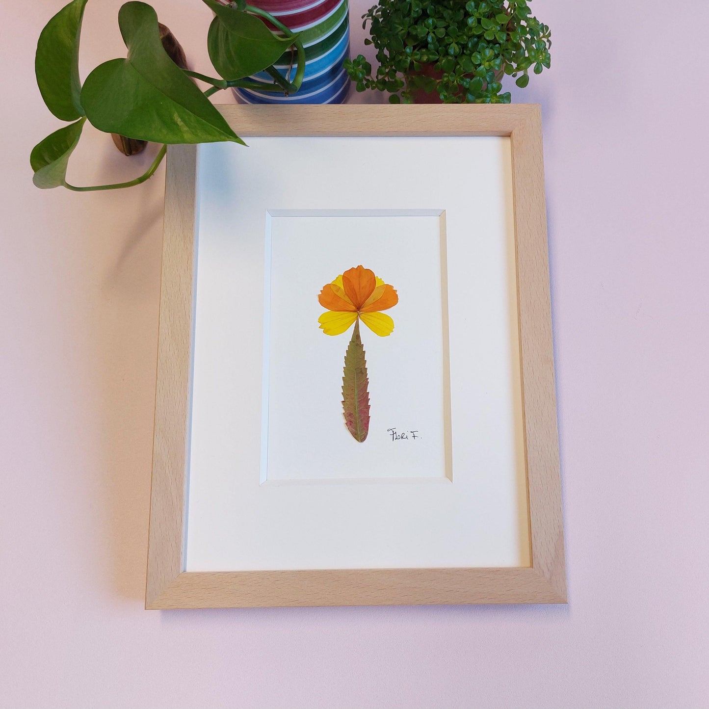 Composition florale minimaliste, réalisée avec des pétales de fleurs de cosmos jaunes et oranges que j'ai cueillis dans les champs fleuris de Luke et Angela de la ferme florale&nbsp;"Au Château Fleuri", située à Schwerdorff en Moselle, France. Ces pétales ont été sublimés par une feuille de sumac de Virginie leur servant de tige, cueillie, elle aussi, en terre mosellane.