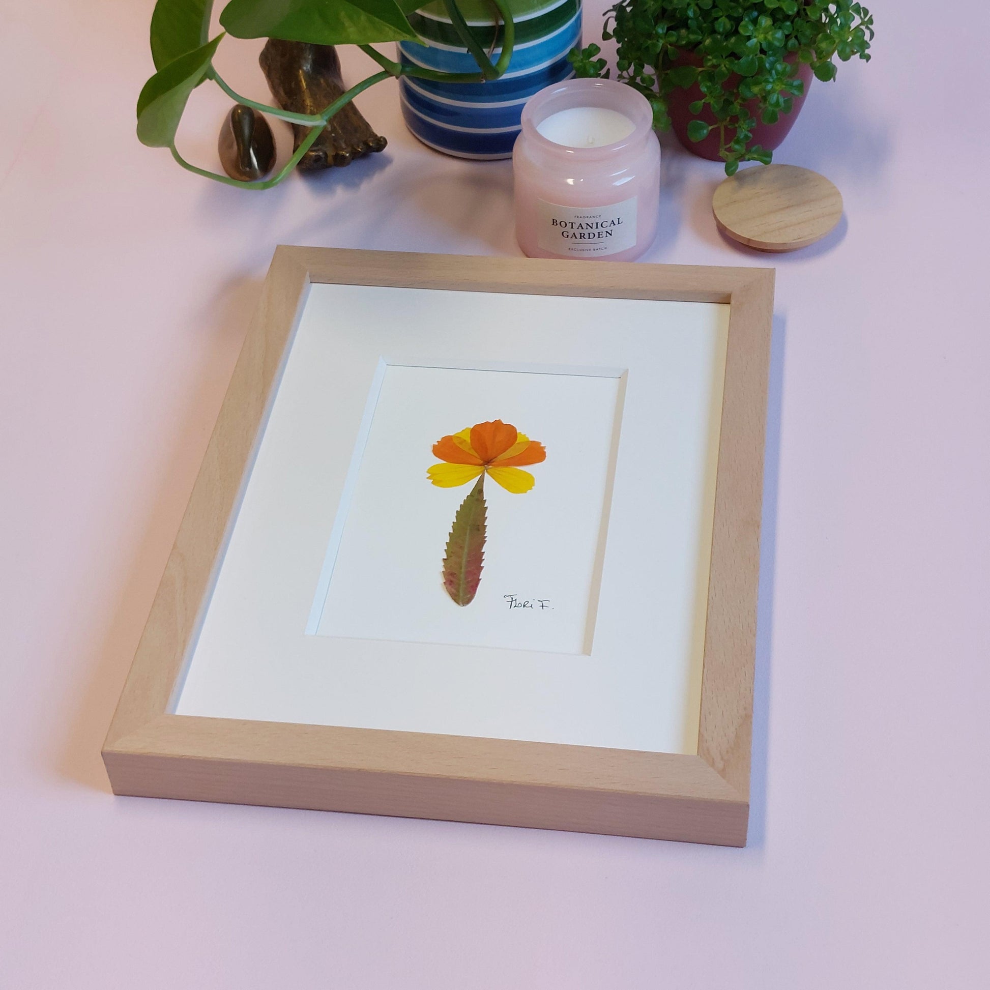 Composition florale minimaliste, réalisée avec des pétales de fleurs de cosmos jaunes et oranges que j'ai cueillis dans les champs fleuris de Luke et Angela de la ferme florale&nbsp;"Au Château Fleuri", située à Schwerdorff en Moselle, France. Ces pétales ont été sublimés par une feuille de sumac de Virginie leur servant de tige, cueillie, elle aussi, en terre mosellane.